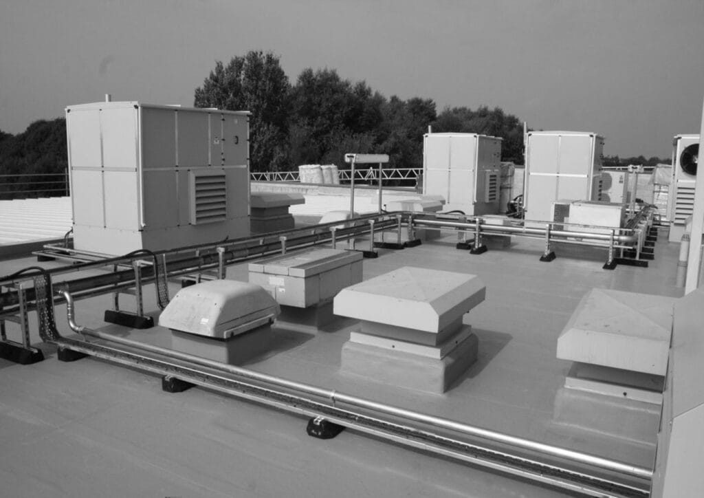 Flat commercial roof with HVAC plant units, ventilation terminals, pipework and cable trays installed on a waterproof membrane roof, illustrating a completed rooftop services installation.